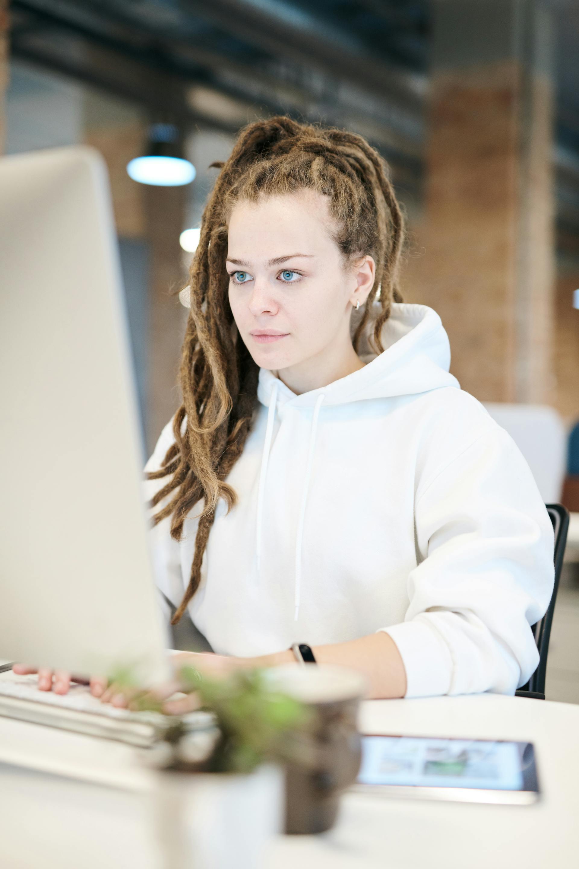 A woman with long braided hair working at a desktop computer.