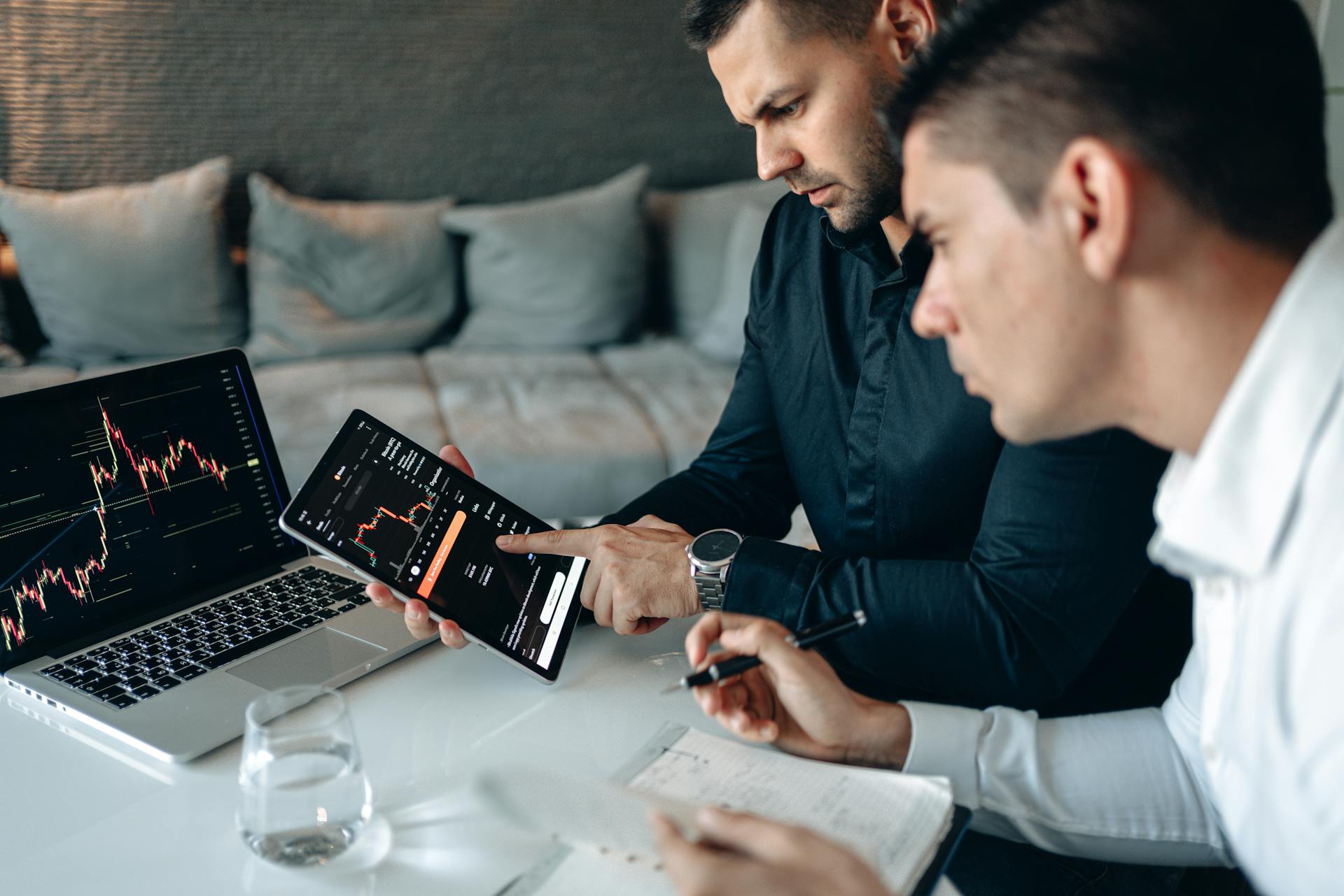 Two men reviewing financial charts on a laptop and a tablet.